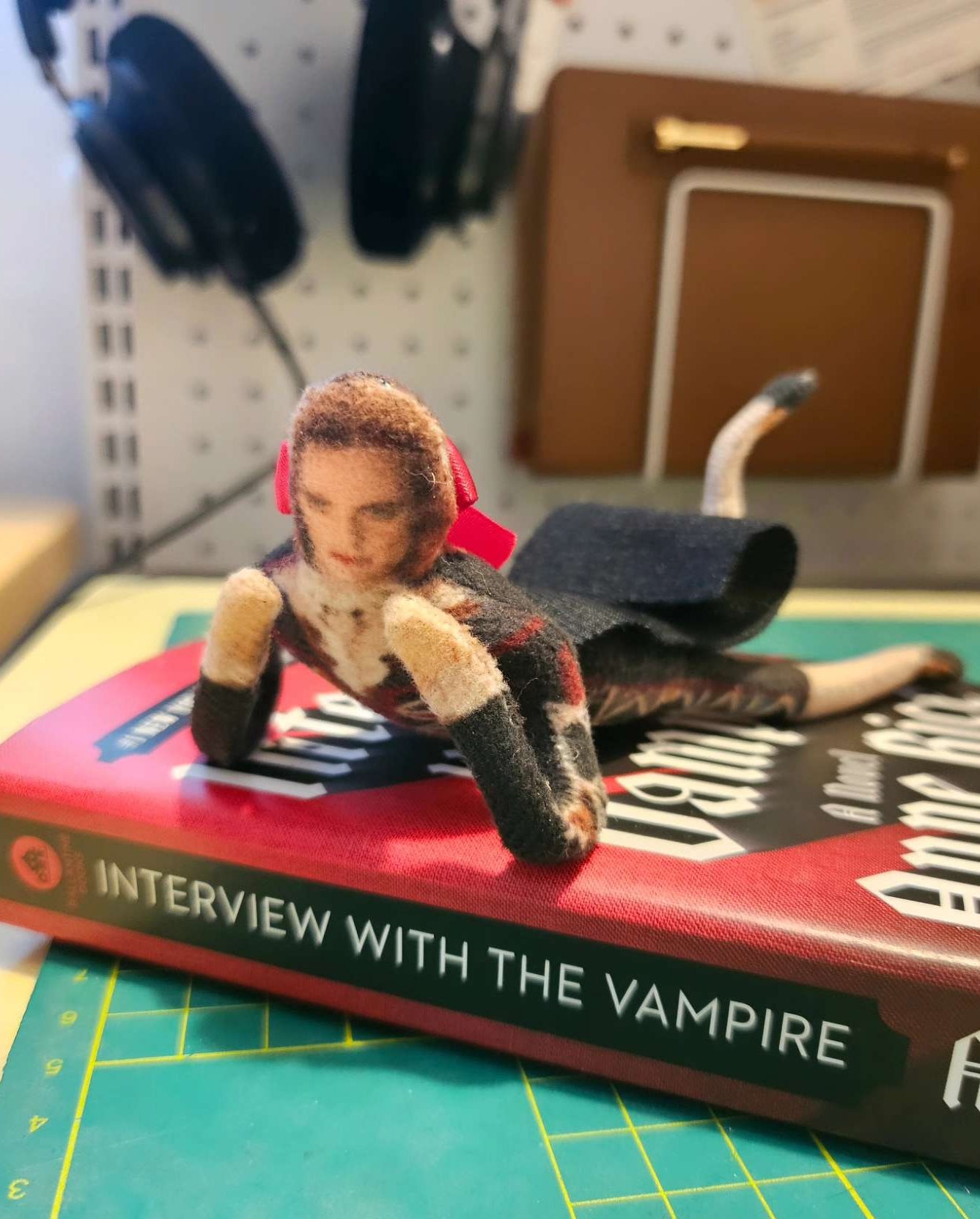 Harlequin Lestat plush figure resting seductively on a paperback cover of 'Interview with the Vampire'.